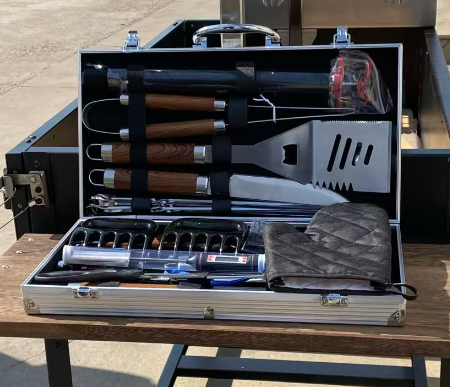 Included grilling tool set in its open hard case, with wooden-handled utensils, skewers and a grilling glove